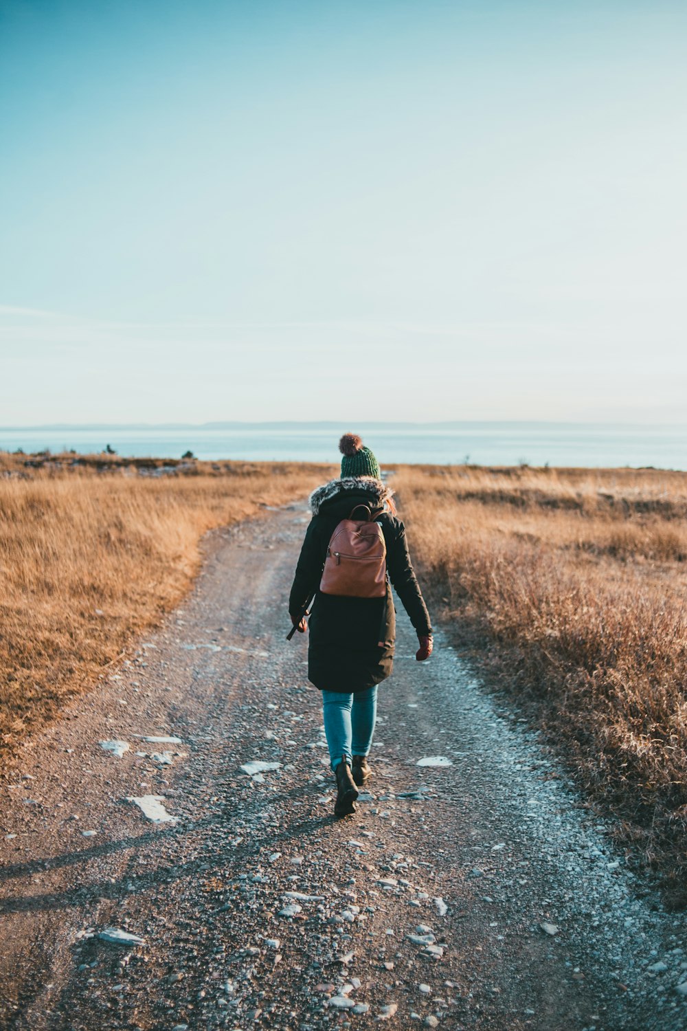 woman in black jacket walking on gray asphalt road during daytime