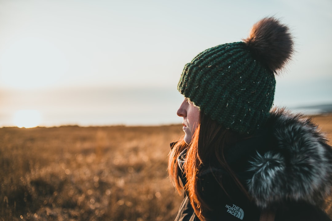 woman in black knit cap and black jacket standing on brown grass field during daytime