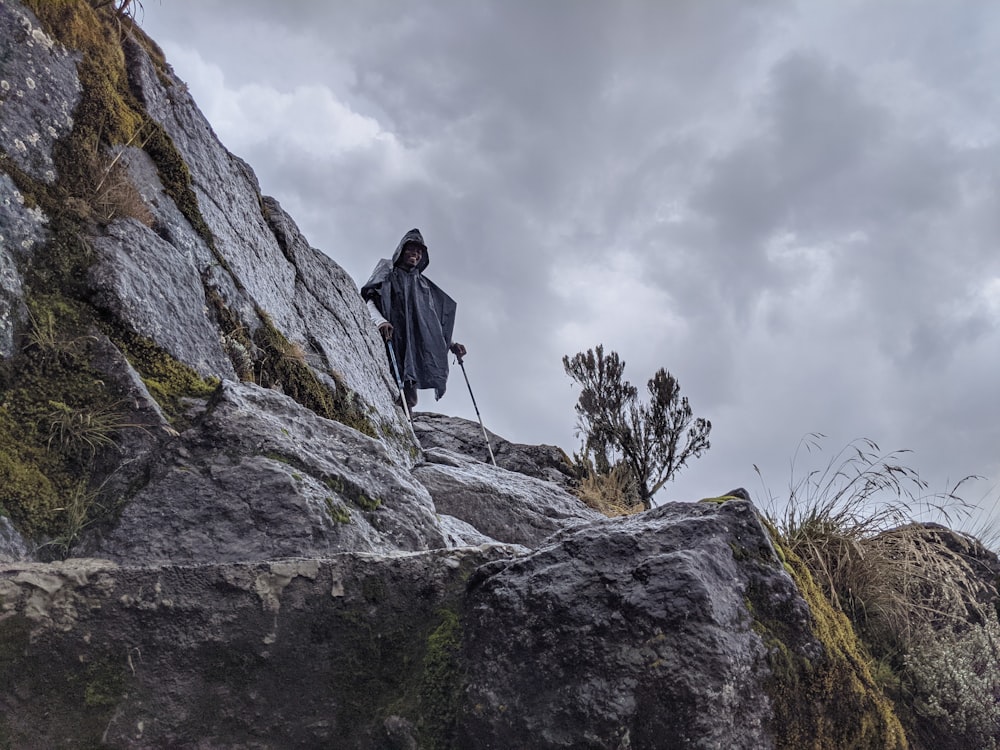 man in black jacket standing on gray rock formation under white cloudy sky during daytime