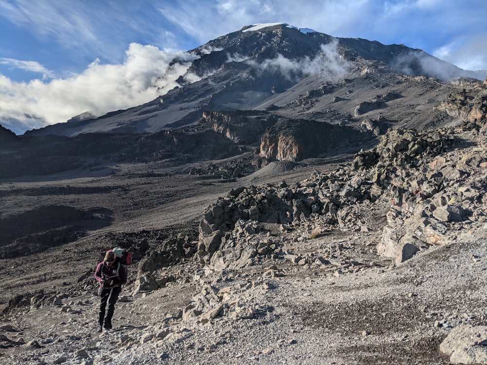 Persona con chaqueta roja y pantalones negros caminando en la montaña rocosa durante el día