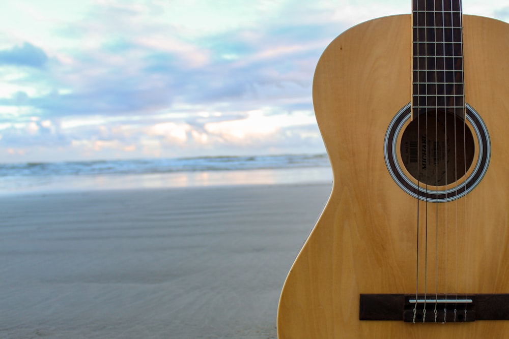 brown acoustic guitar on beach during daytime