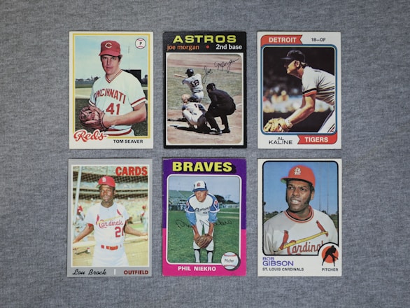 A collection of six vintage baseball cards featuring players from different teams, neatly arranged on a gray surface. Each card displays a portrait or action shot of a player, along with their team name and position.