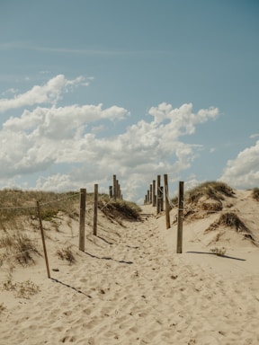 clôture en bois marron sur sable brun sous un ciel bleu et des nuages ​​blancs pendant la journée