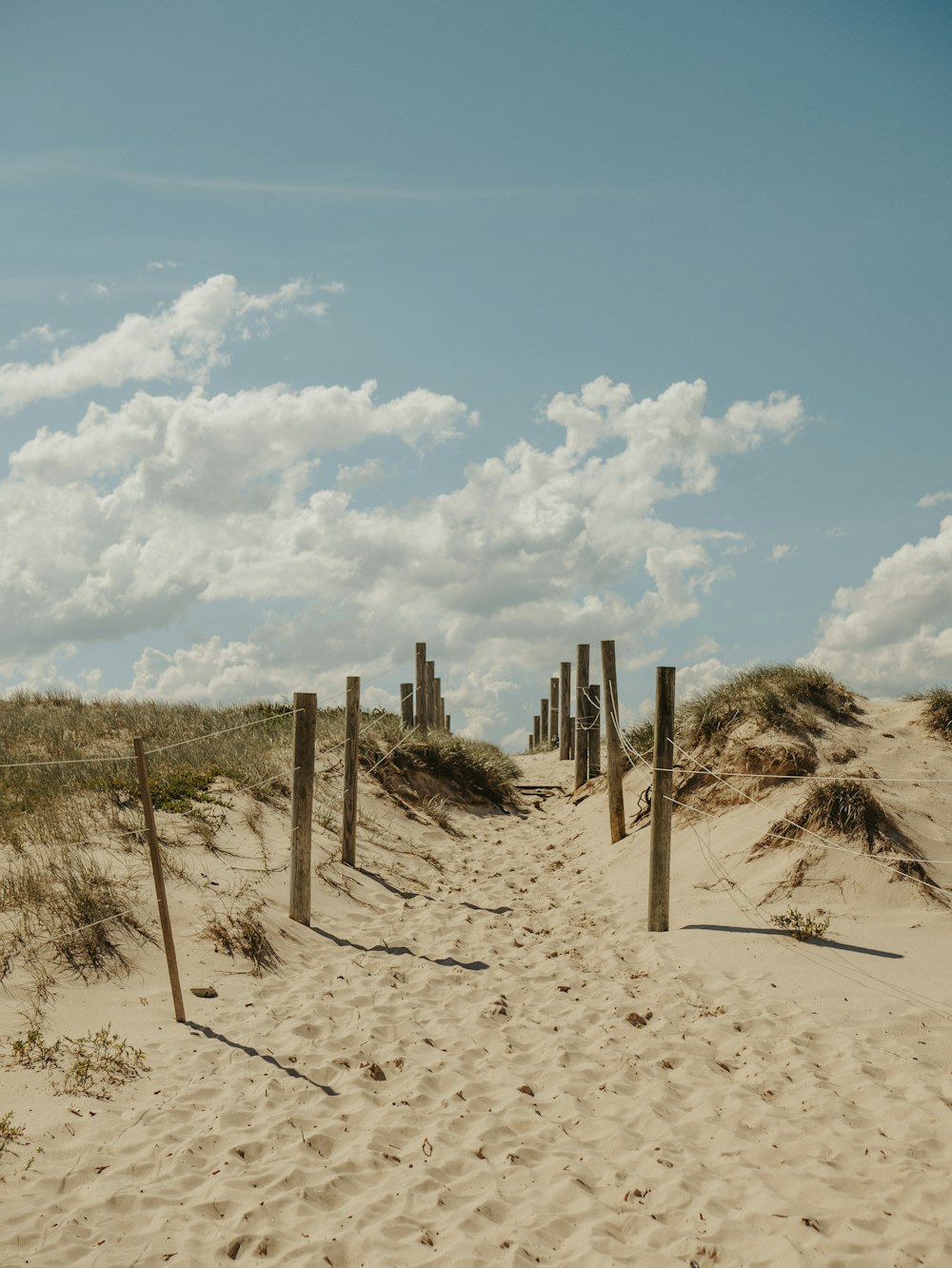 staccionata di legno marrone su sabbia marrone sotto cielo blu e nuvole bianche durante il giorno