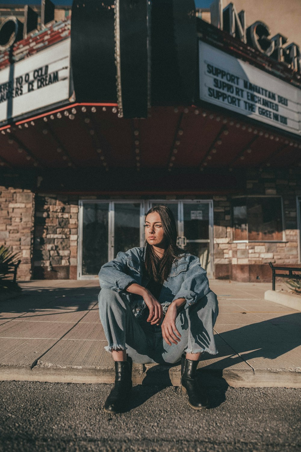 woman in gray coat sitting on sidewalk during daytime