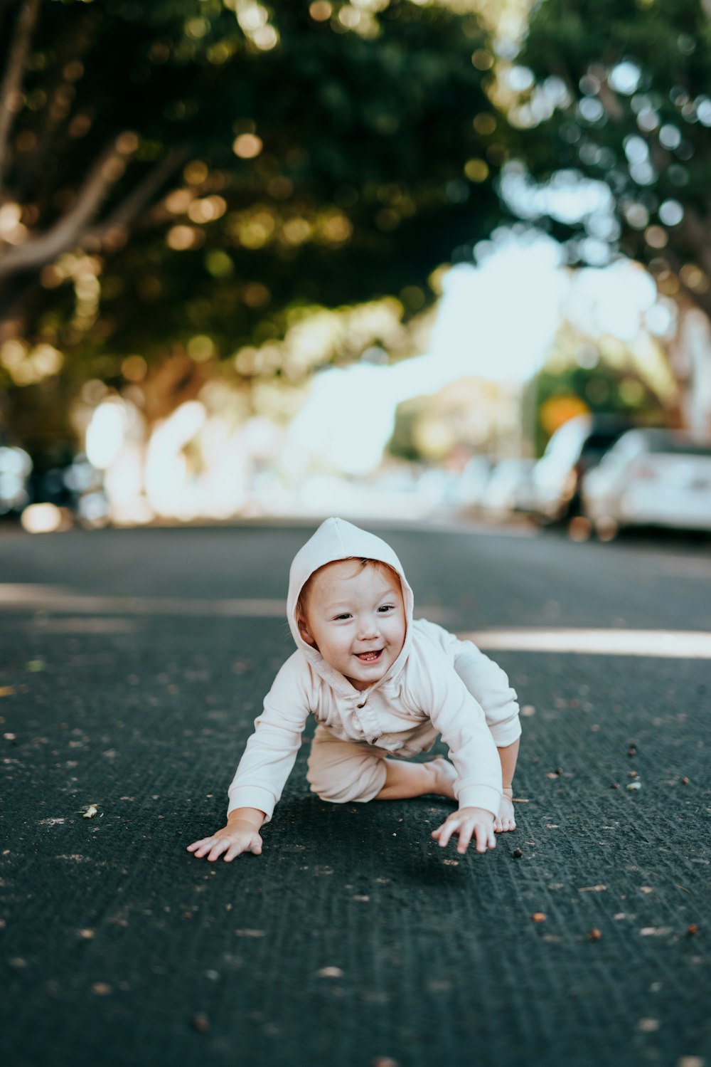 白い長袖シャツと白い帽子をかぶった赤ちゃんが昼間、道路に座っている