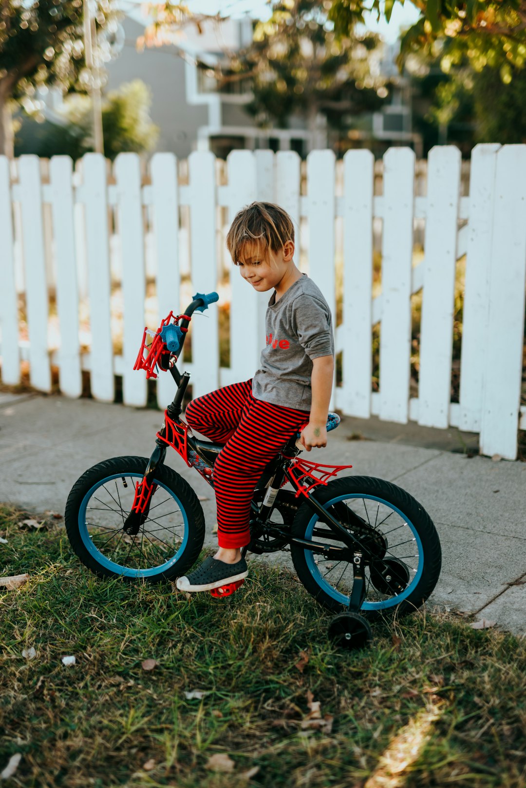 girl in red and black bicycle suit standing beside white wooden fence during daytime