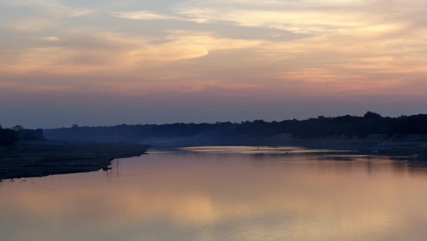 A serene sunrise over a quiet river, reflecting soft shades of red in the sky.