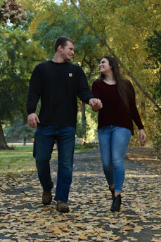 Novios caminando de la mano en un parque, sonriendo y disfrutando su historia juntos.