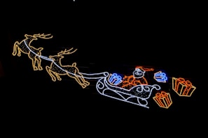 Santa waving goodbye from a sleigh, with festive lights glowing in the background.