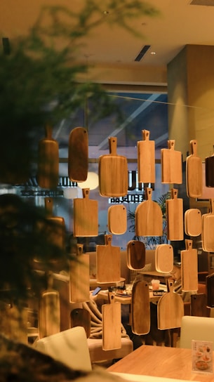 A series of wooden cutting boards are suspended in front of a cozy restaurant interior, soft lighting illuminating the warm wooden tones. Behind the boards, seating areas with plush chairs and tables can be seen.