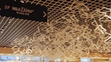 A ceiling installation made up of numerous white hangers is seen in a modern interior space. The hangers are artfully arranged to create an intricate pattern. A sign for the MUJI Diner located on the second floor is visible, written in both English and Japanese.