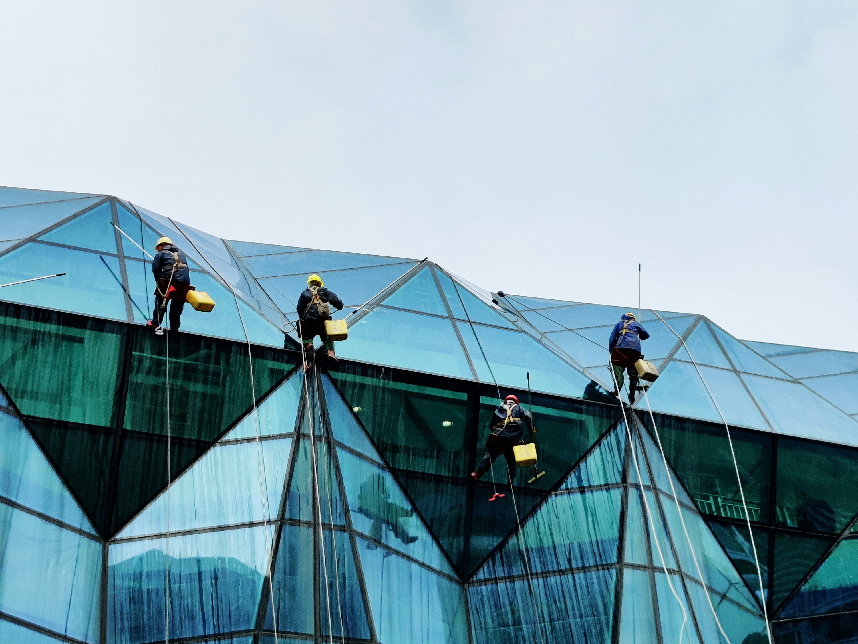 man in yellow jacket and black pants standing on blue building during daytime
