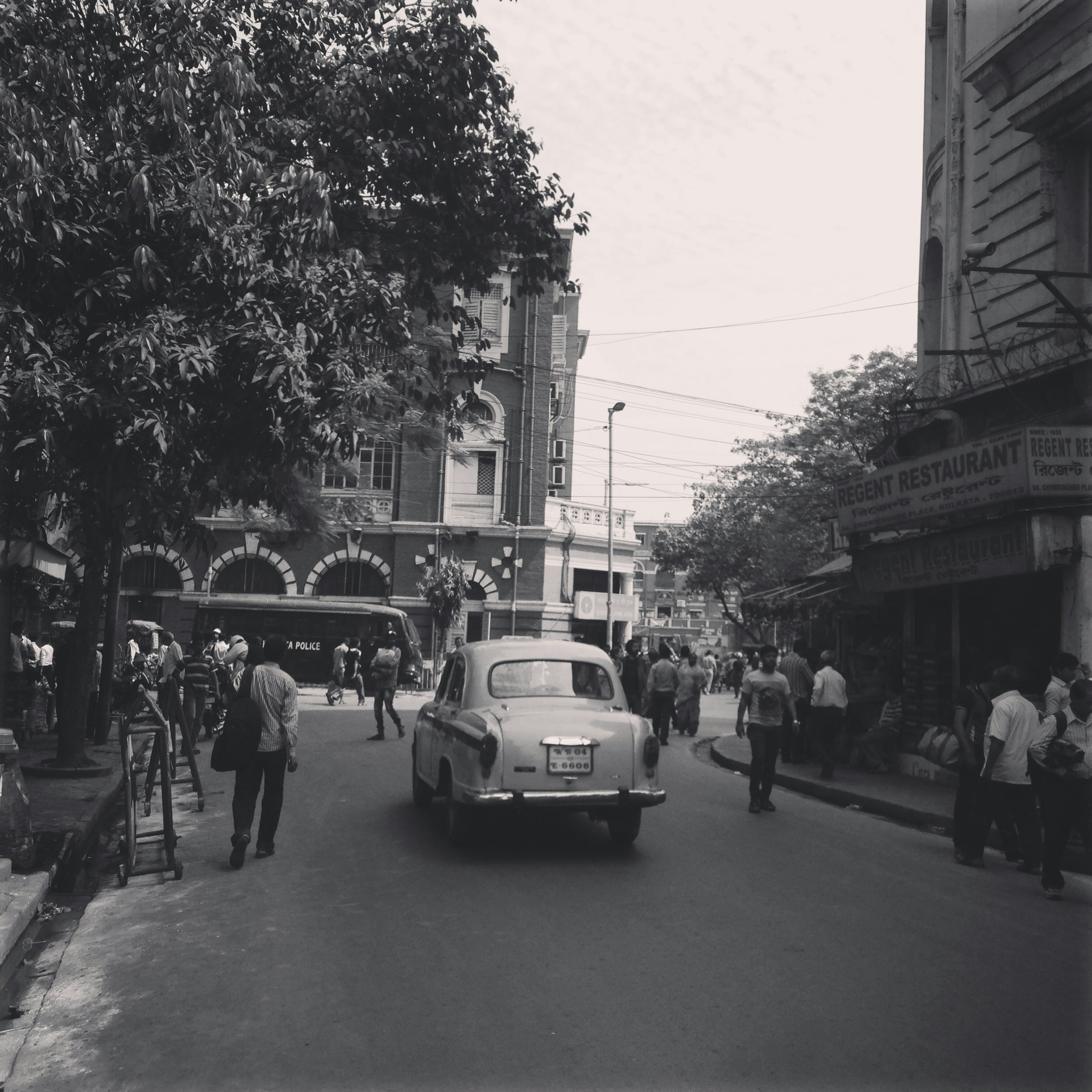 grayscale photo of people walking on sidewalk near cars and buildings
