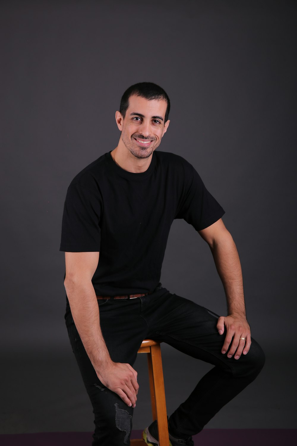 man in black crew neck t-shirt and black pants sitting on brown wooden seat