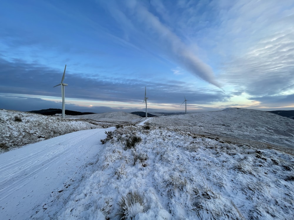 turbine eoliche bianche su terreno coperto di neve sotto cielo blu durante il giorno