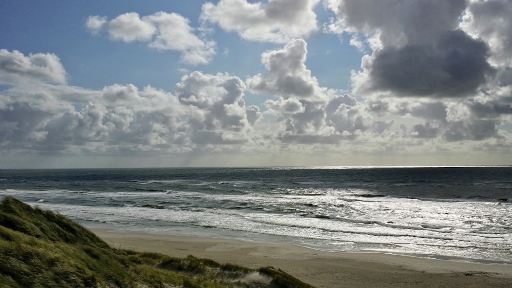 sea waves crashing on shore under white clouds and blue sky during daytime