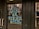 Large, bold blue and yellow letters on a glass door read 'Buy Local or Bye-Bye Local', reflecting a street scene with buildings and pedestrians in the background.