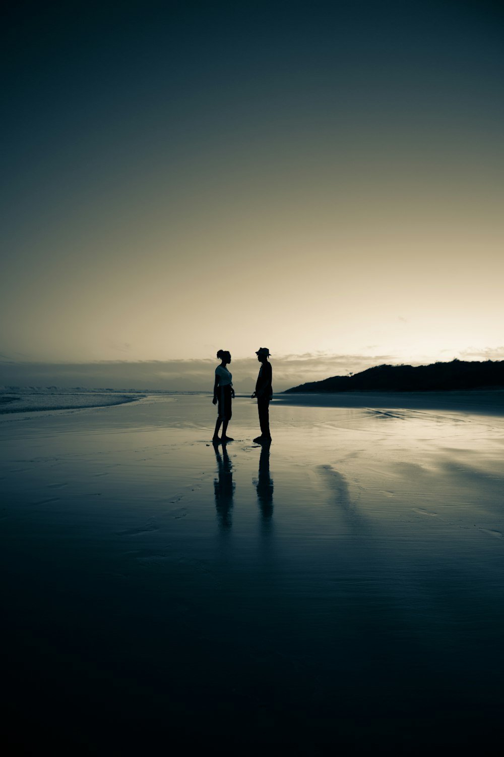 silhouette of man and woman standing on seashore during sunset