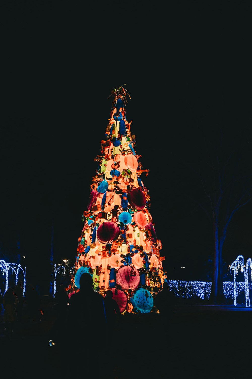 people standing near lighted christmas tree during night time