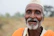 A warm portrait of a smiling tribal elder standing in a lush green forest clearing.