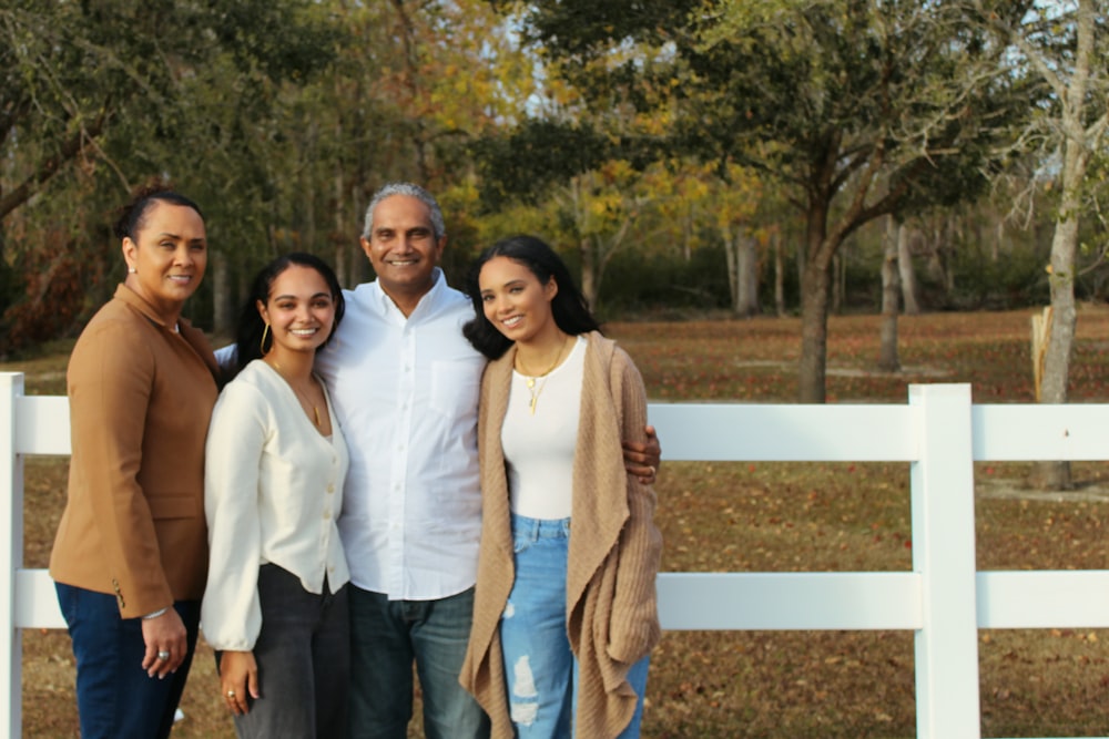 2 women and man standing beside white wooden fence during daytime