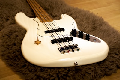 Close-up of a sleek bass guitar resting on a wooden floor with warm lighting.