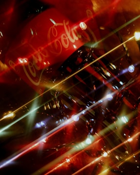 A vibrant display with a Coca-Cola sign, surrounded by an array of shimmering lights and reflections. The composition creates a dynamic and festive atmosphere.