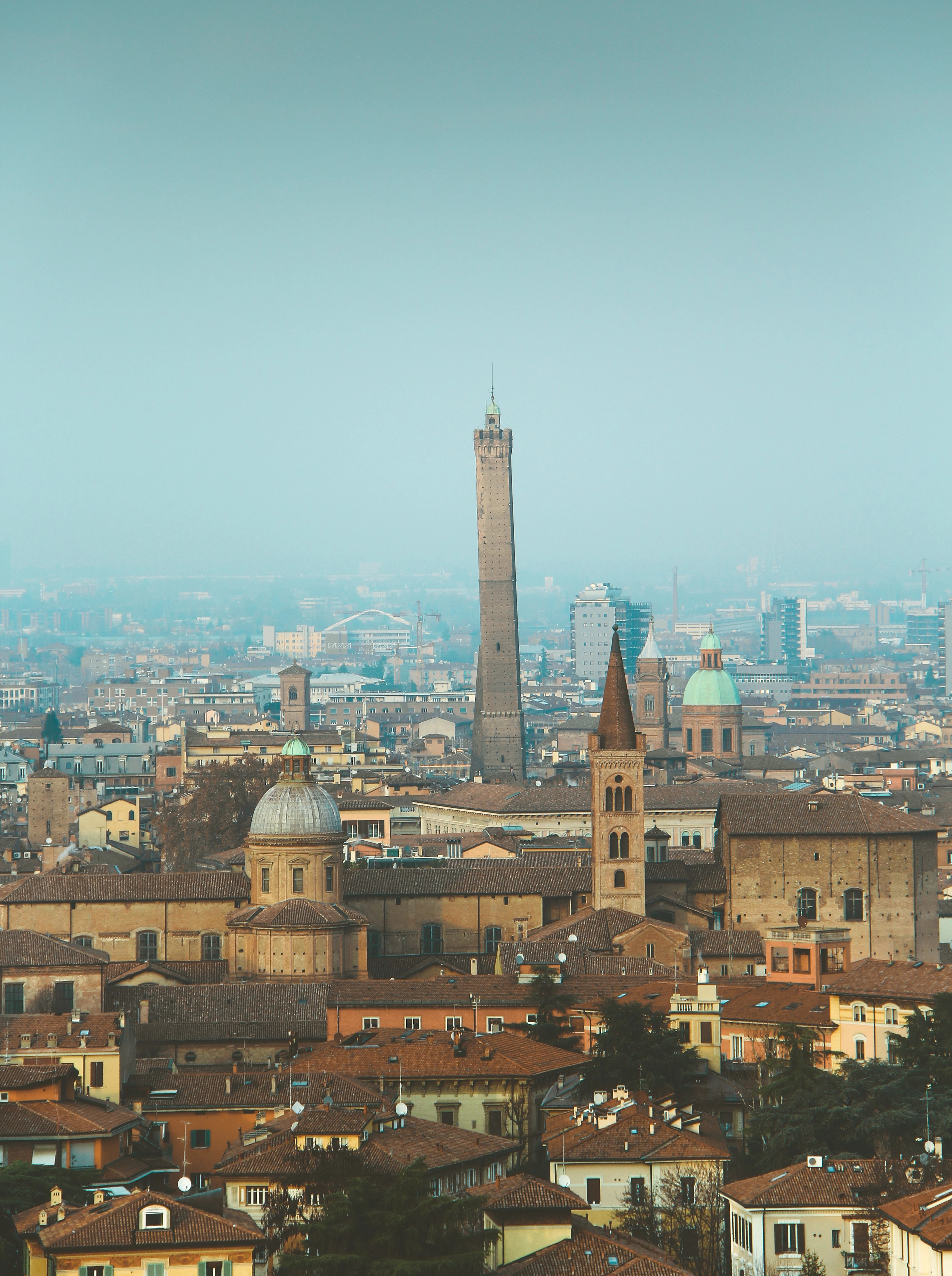 Bologna's terracotta rooftops in haze, the leaning Asinelli tower rising over the domes and campanili
