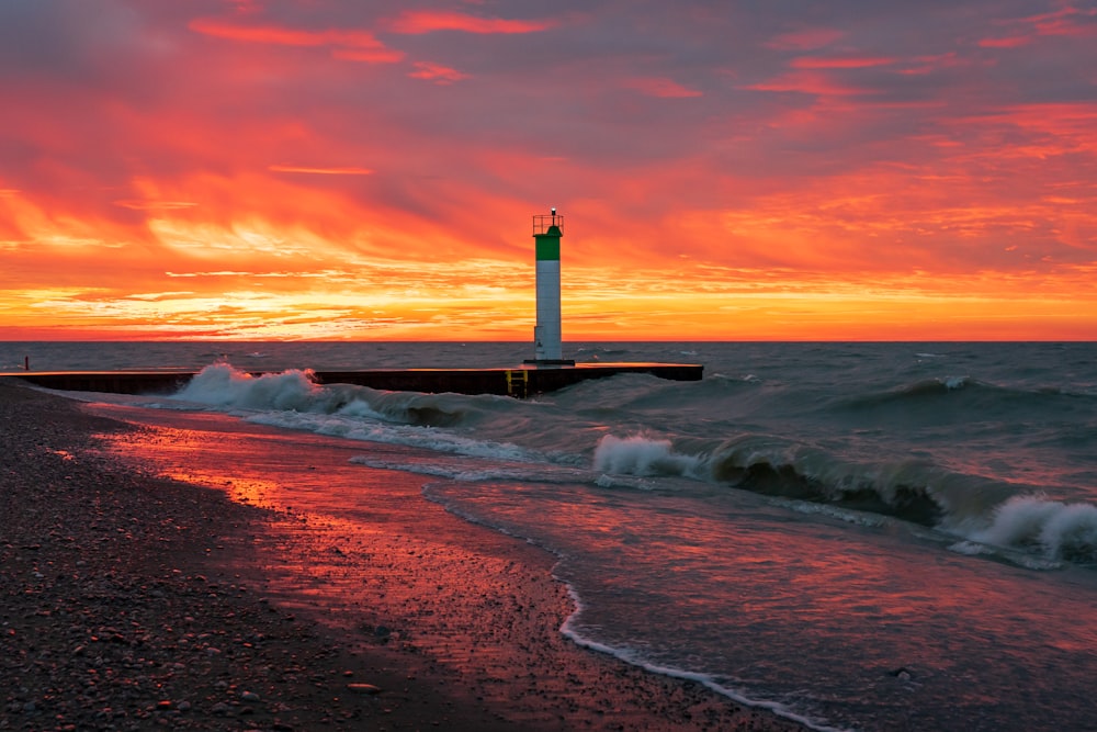white and black lighthouse on seashore during sunset