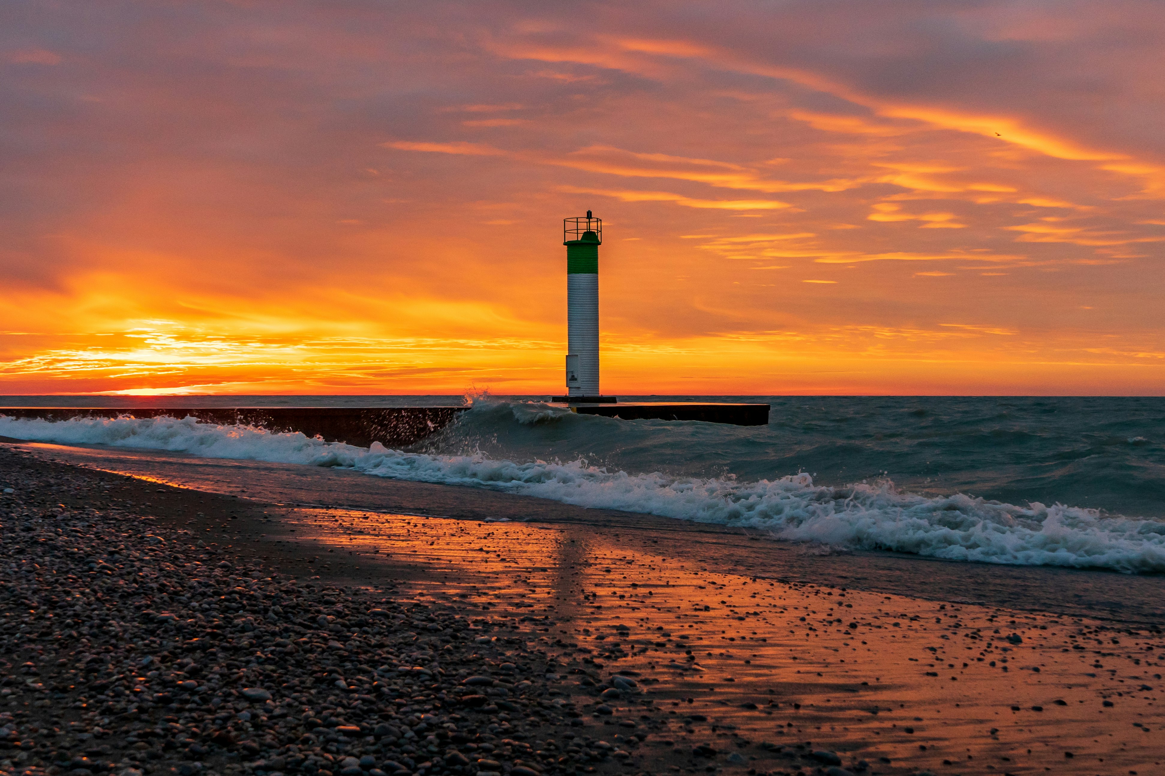 white and black lighthouse on beach during sunset