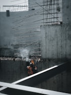 man in orange jacket sitting on the edge of a building