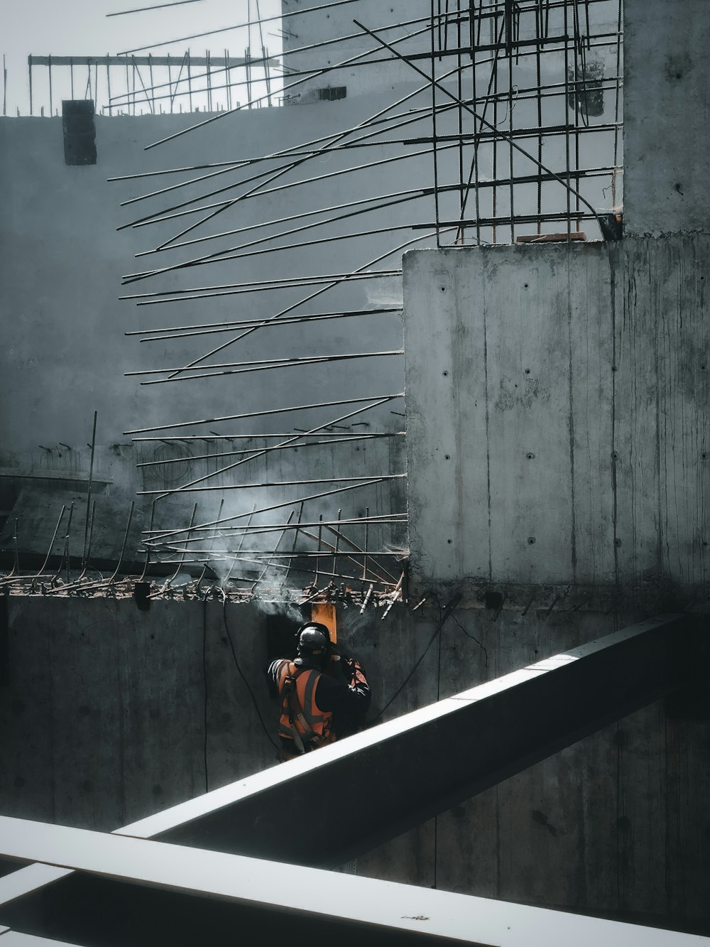 man in orange jacket sitting on the edge of a building