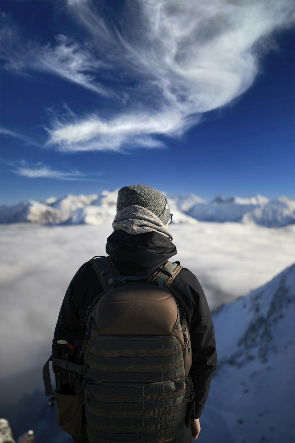 person in gray knit cap and black backpack looking at snow covered mountain during daytime