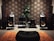 A cozy room featuring an elaborate audio setup with large speakers, audio equipment, and a decorative pattern on the wall. A leafy potted plant adds a touch of greenery. An orange shag rug and a black cushioned seat are positioned in the foreground.