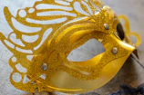An elegant mask resting on a glass surface reflecting subtle gold highlights.