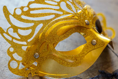 An elegant mask resting on a glass surface reflecting subtle gold highlights.