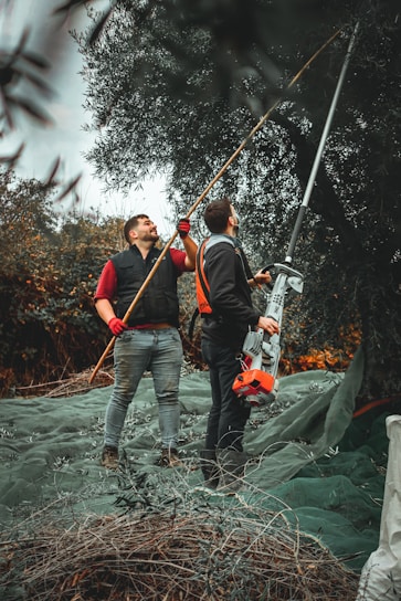 2 men in blue denim jeans and orange jacket holding brown wooden stick during daytime