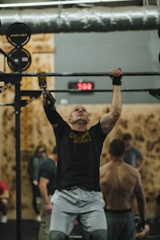 man in black crew neck t-shirt and gray shorts holding black metal bar