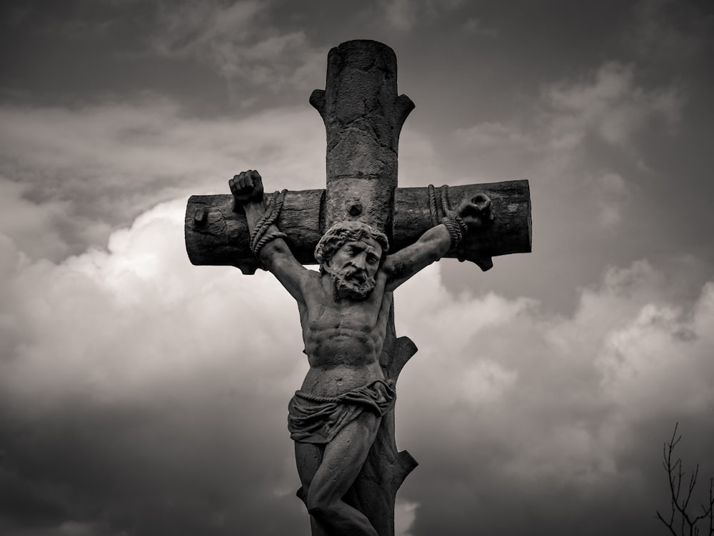 grayscale photo of man holding cross statue