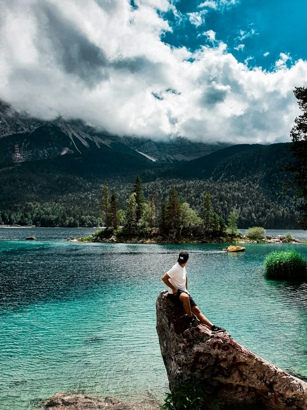 woman in white tank top sitting on rock near lake during daytime