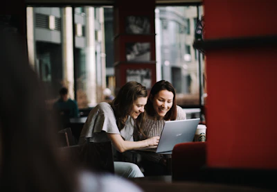 Two people laughing together while looking at a shared screen in a cozy café.