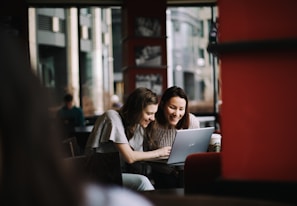 A cozy coffee shop scene where two friends share a laugh while browsing deals on a tablet.