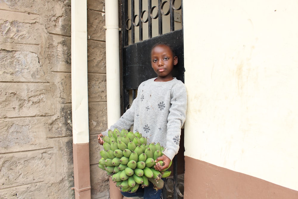 woman in gray sweater standing beside green fruits