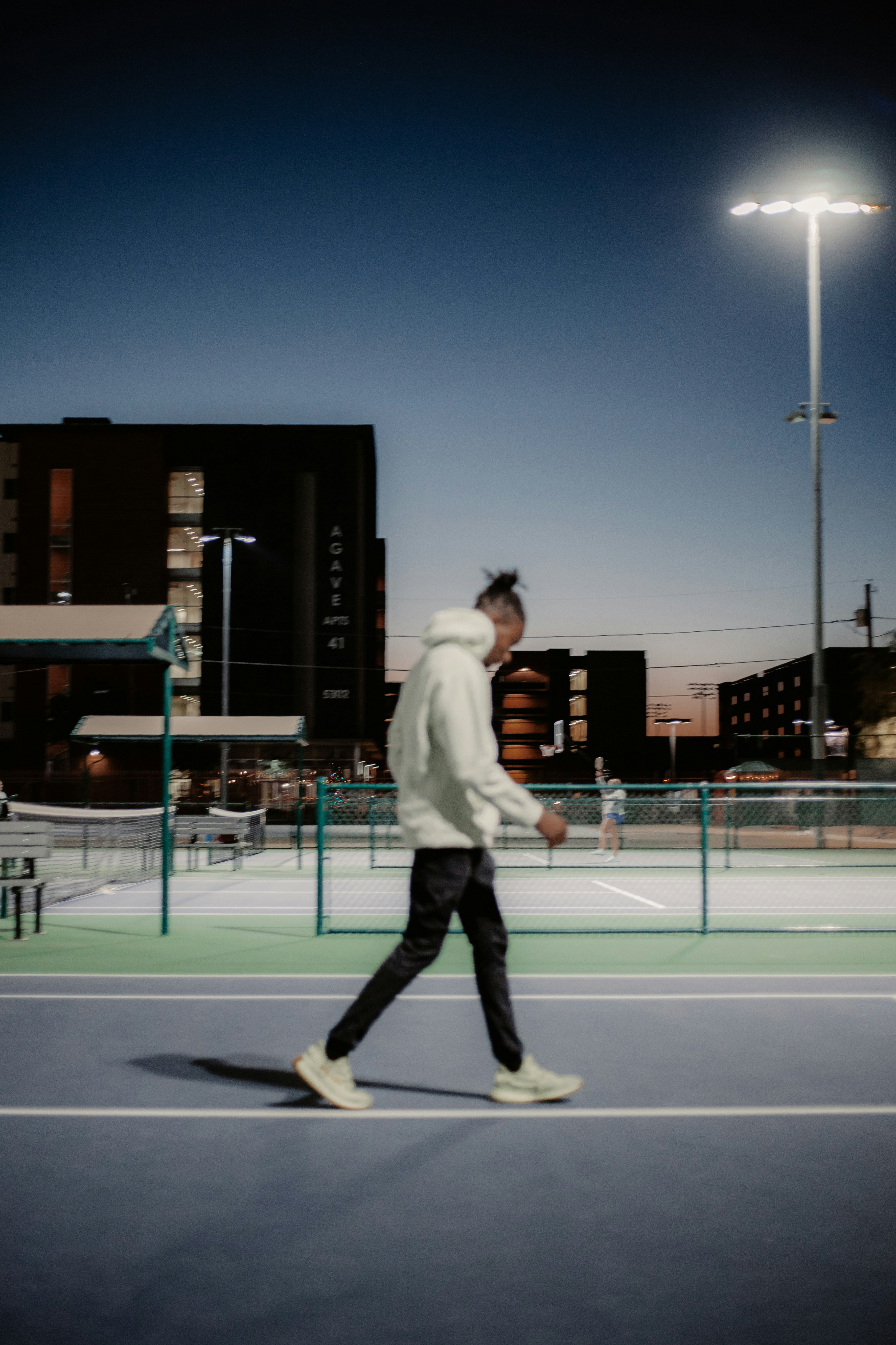 白い長袖シャツと黒いズボンを着た男性が昼間、バスケットボールコートに立つ