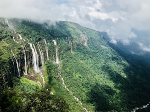 waterfalls on green mountain under white clouds during daytime