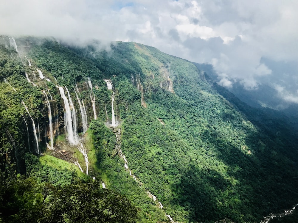 waterfalls on green mountain under white clouds during daytime