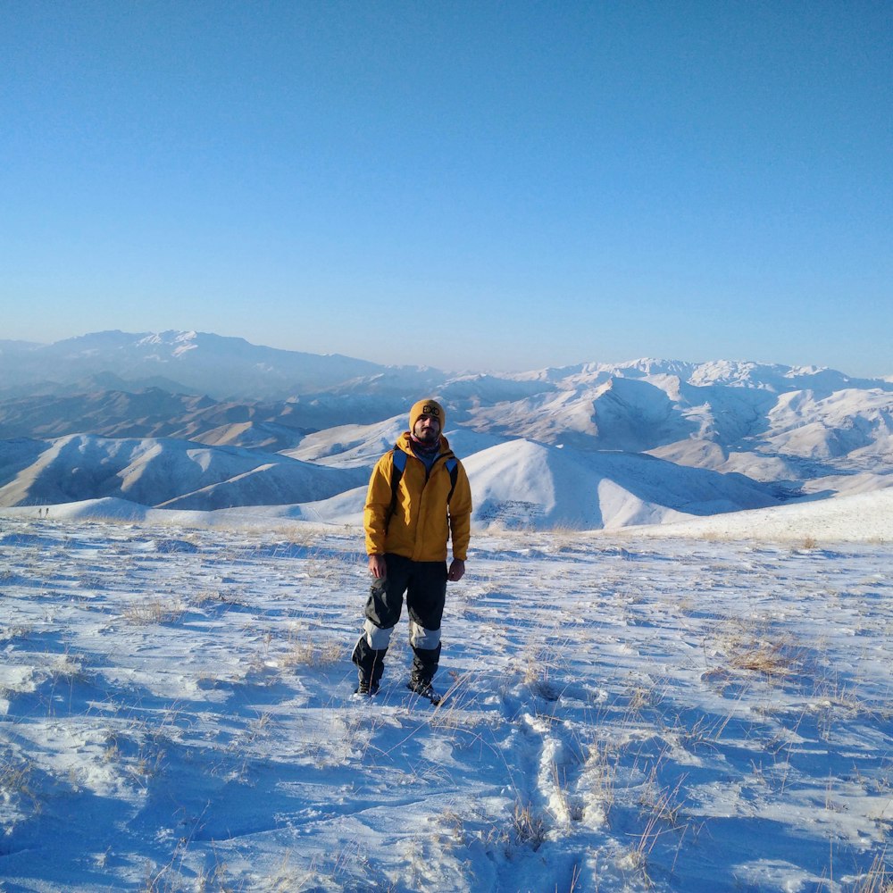 man in brown jacket and black pants standing on snow covered ground during daytime