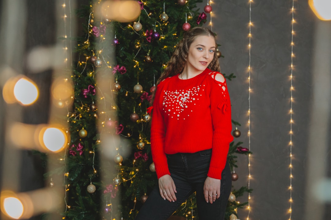 girl in red sweater standing beside christmas tree