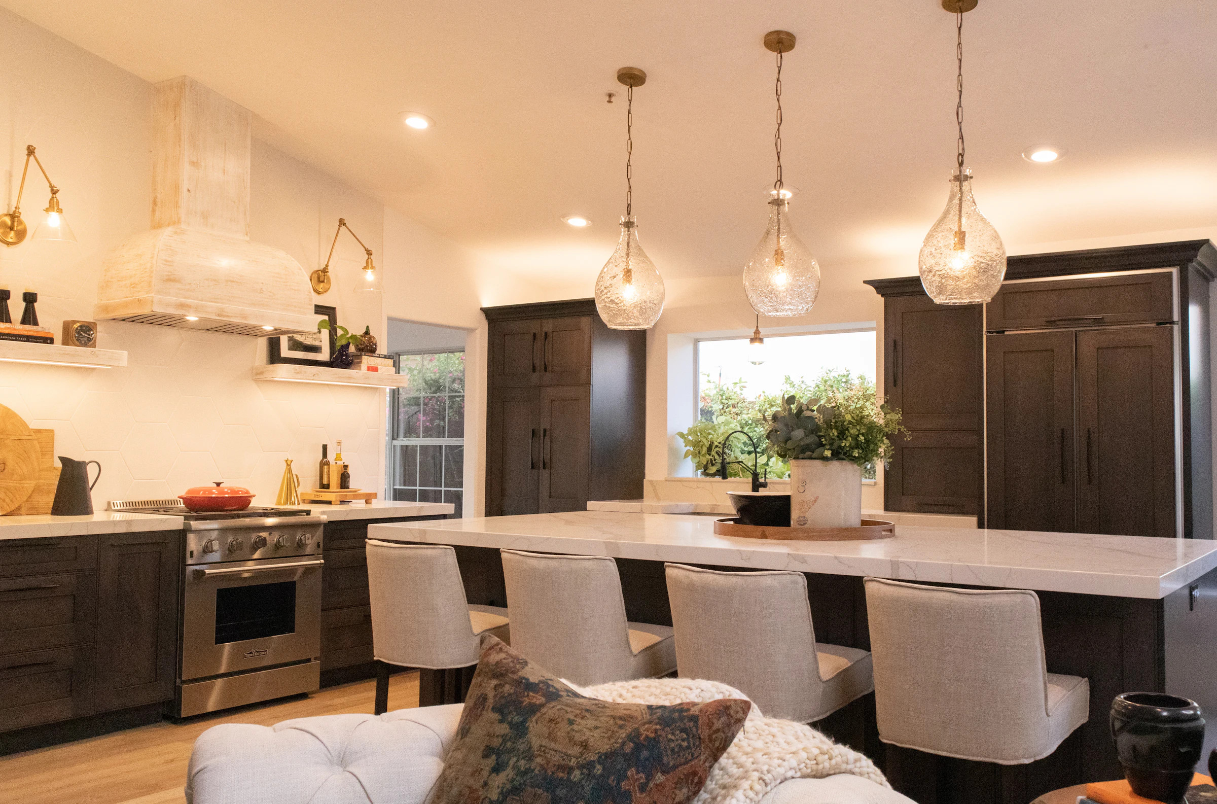 Warm kitchen lit by three glass pendant lights over a long island